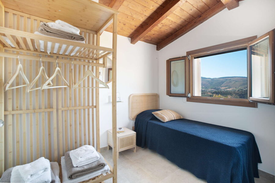 Charming single bedroom at Villa Belvedere, a Sicily luxury villa with pool, featuring wooden beams, natural décor, and stunning countryside views.