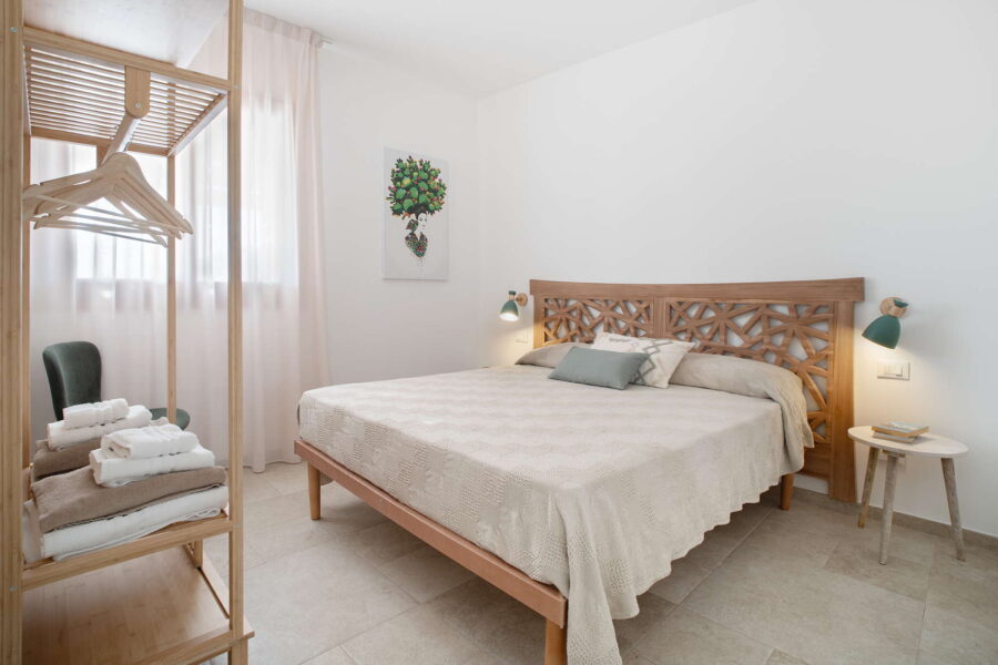 Cozy and stylish bedroom at Villa Belvedere, a Sicily luxury villa with pool, featuring a carved wooden headboard, soft linens, and natural light.