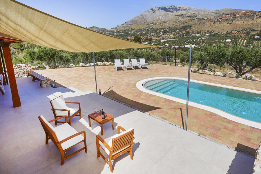 Spacious poolside terrace with shaded seating, sun loungers, and panoramic mountain views at Villa Pietra Dorata, Sicily.