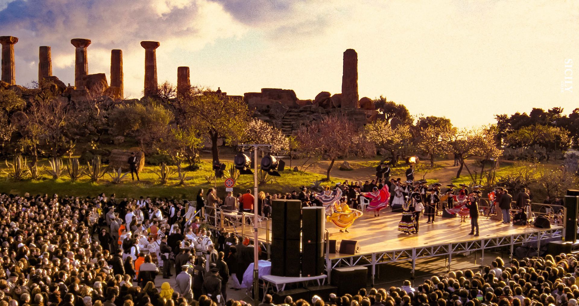 Traditional dance performance at the Almond Blossom Festival in the Valley of the Temples, Agrigento, Sicily, with ancient Greek ruins and blooming almond trees in the background.